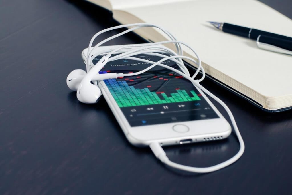 Music app on the iPhone 6 screen with EarPods, notebook and pen