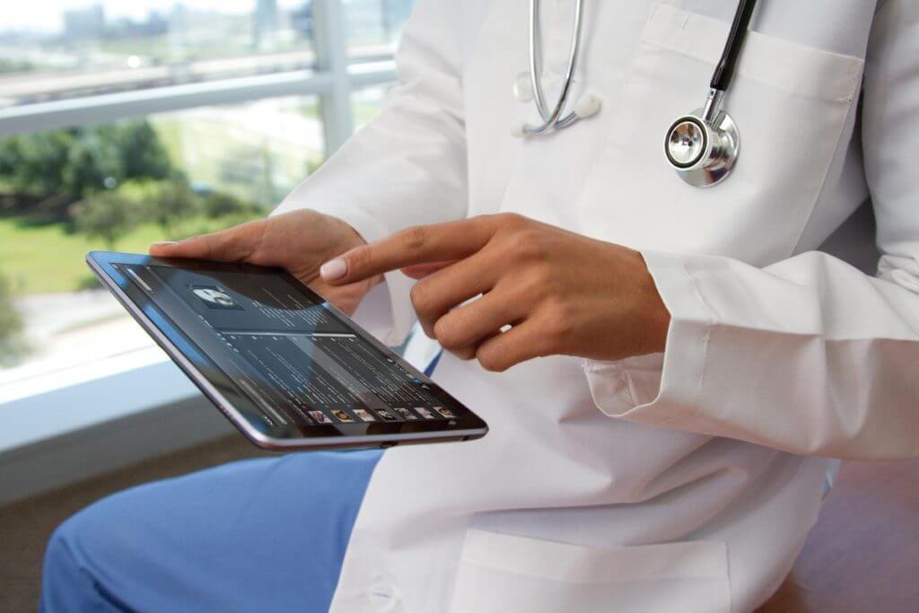 The doctor's hands hold a tablet with a medical app on the screen