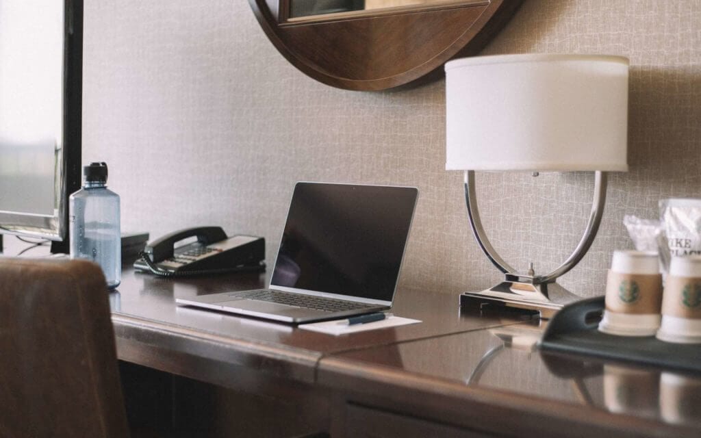 Laptop, phone, lamp, bottle and coffee cups on the desk in the hotel room